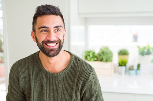 Man in green sweater in a white kitchen smiling