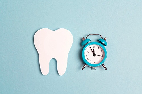 Cutout tooth next to a small blue alarm clock on a pale blue background