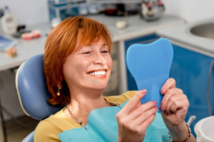 Woman sitting in dental chair and admiring new dentures