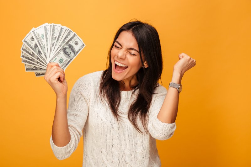 Patient holding money and smiling with their dental implants